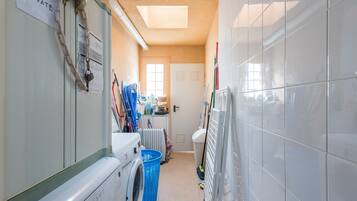 A narrow laundry room with a washing machine, a dryer, a blue laundry basket, and a radiator.