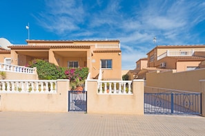 A residential building with a tiled roof, a gated entrance, and a balcony with railings.