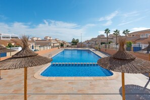 Una piscina con agua cristalina azul, rodeada de palmeras y un solárium con baldosas.