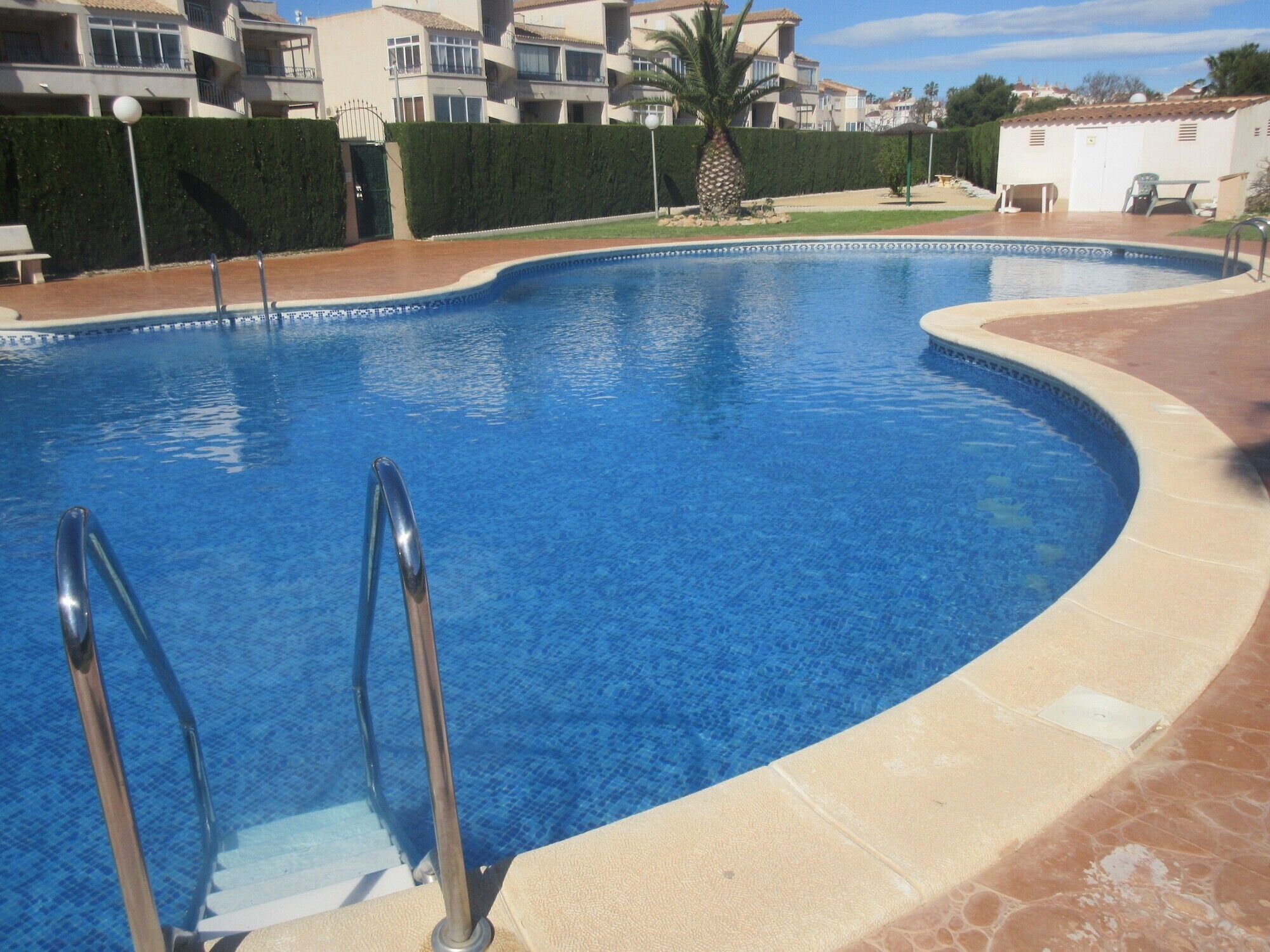 Una piscina con borde curvo, barandillas metálicas y un deck con baldosas a su alrededor.
