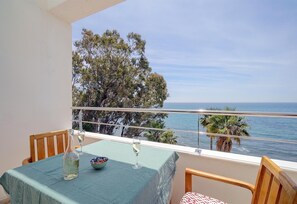 Un balcon avec une table dressée pour deux personnes, donnant sur une étendue d’eau et des arbres.