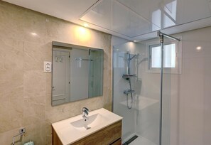 Une salle de bain moderne avec un mur en marbre, un lavabo blanc, une douche en verre et un miroir.