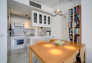 Een moderne keuken met witte kastjes, een eettafel met stoelen, een boekenkast en een hanglamp.