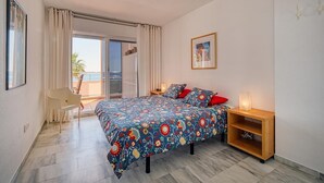 Una camera da letto con un letto, un comodino, una sedia, una porta finestra e un quadro appeso al muro.