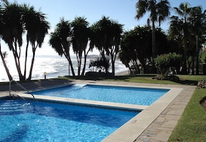 A pool with a view of the ocean, surrounded by palm trees and a clear sky. - Apartment "Boulevard 305" with Sea View, Pool, Wi-Fi, Balcony, Terrace & Garden (Estepona)