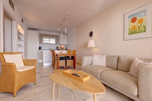 A living room with a sofa, armchair, coffee table, and a dining area with chairs and a table.