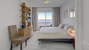 Een slaapkamer met een bed, een boekenkast, een stoel en uitzicht op zee.