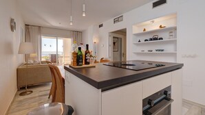 Een moderne keuken met een centraal eiland, inbouwplanken en een zithoek met een bank en lamp.