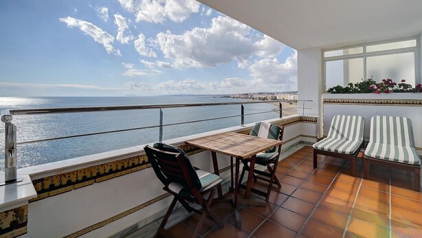 Een balkon met een tafel, stoelen, een hekwerk en uitzicht op zee.