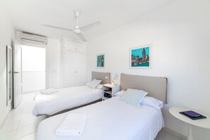 Een hotelkamer met twee bedden, een plafondventilator, een nachtkastje met een boek en kunst aan de muur.