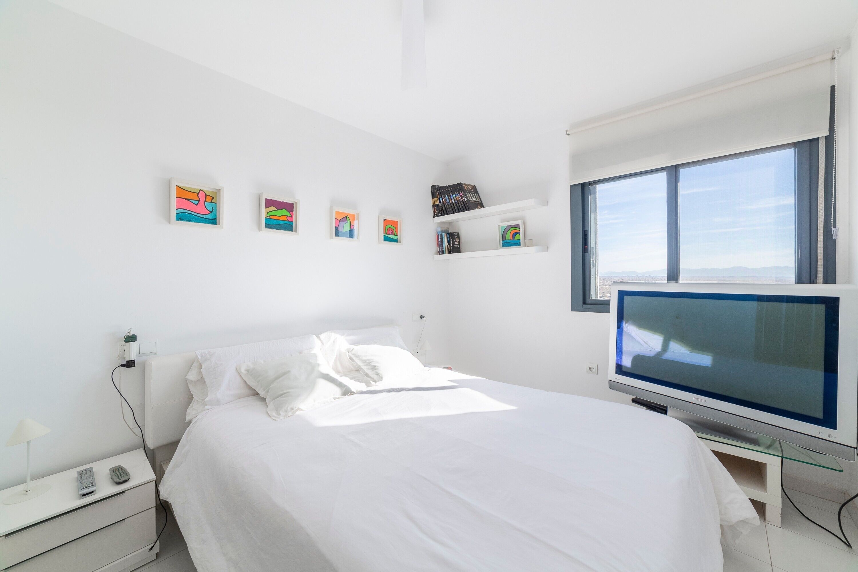 Ein Schlafzimmer mit Bett, Fernseher, Nachttisch und einem Kunstwerk an der Wand.