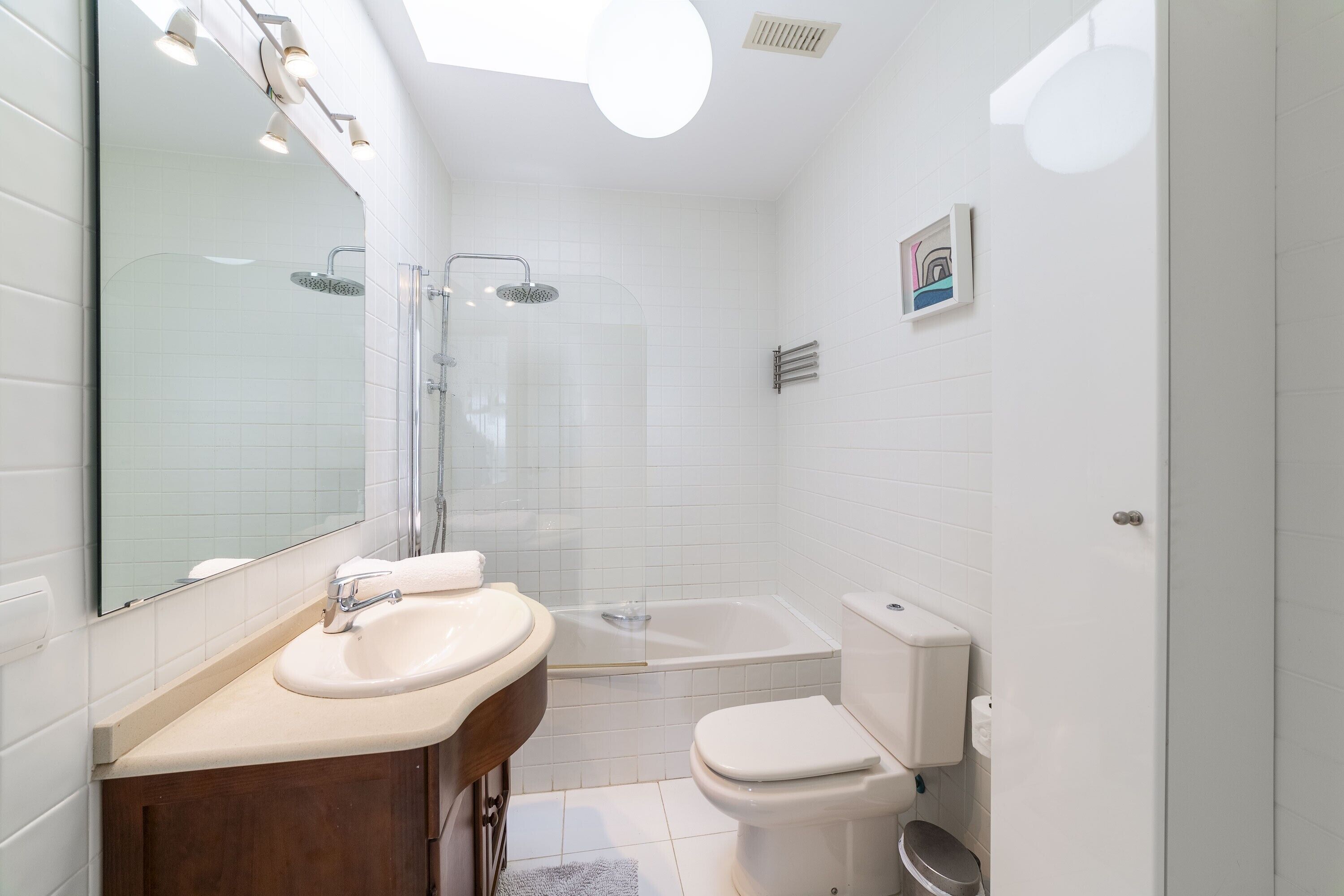 A modern bathroom with a sink, mirror, shower, and toilet.