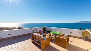 Eine Terrasse mit Holzmöbeln, einem grünen Tisch und Blick auf das Meer.