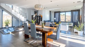 Ein modernes Interieur mit Essbereich, Treppe und Wohnbereich mit großen Fenstern.