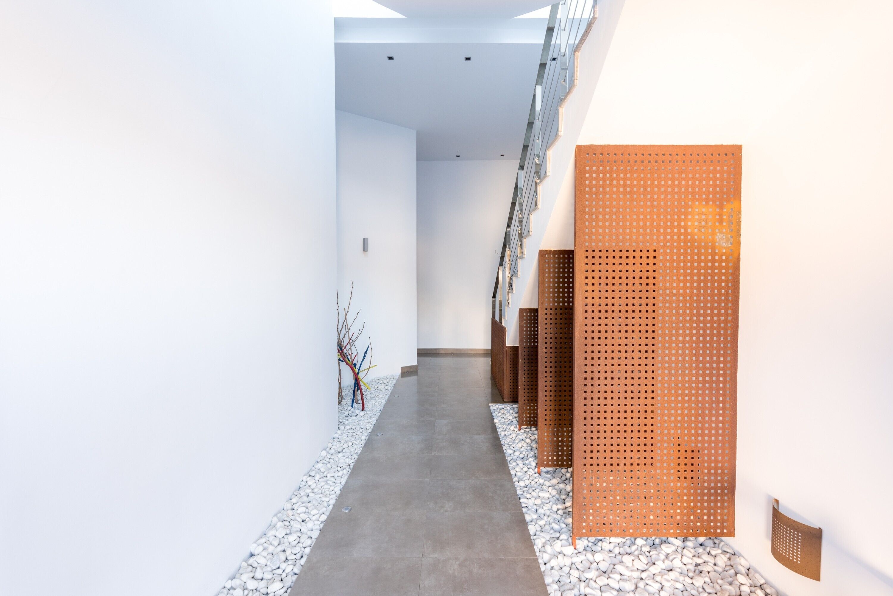 A modern interior with a concrete pathway, white walls, and a wooden perforated panel.