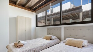 Ein Zimmer mit zwei Betten, einem Kleiderschrank und einem großen Fenster mit Blick ins Innere des Gebäudes.