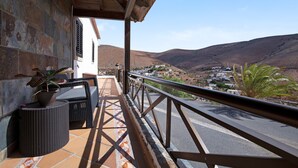 Ein Balkon mit Korbmöbeln, einer Topfpflanze und Blick auf ein Tal mit Gebäuden.