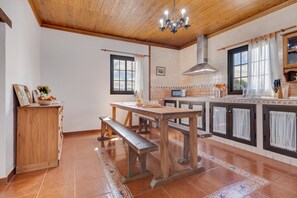 A kitchen with wooden cabinets, a wooden dining table, a bench, a chandelier, and a tiled floor. - Holiday Home "Villa Antonia" with Pool, Wi-Fi, Terraces and Garden (Betancuria)