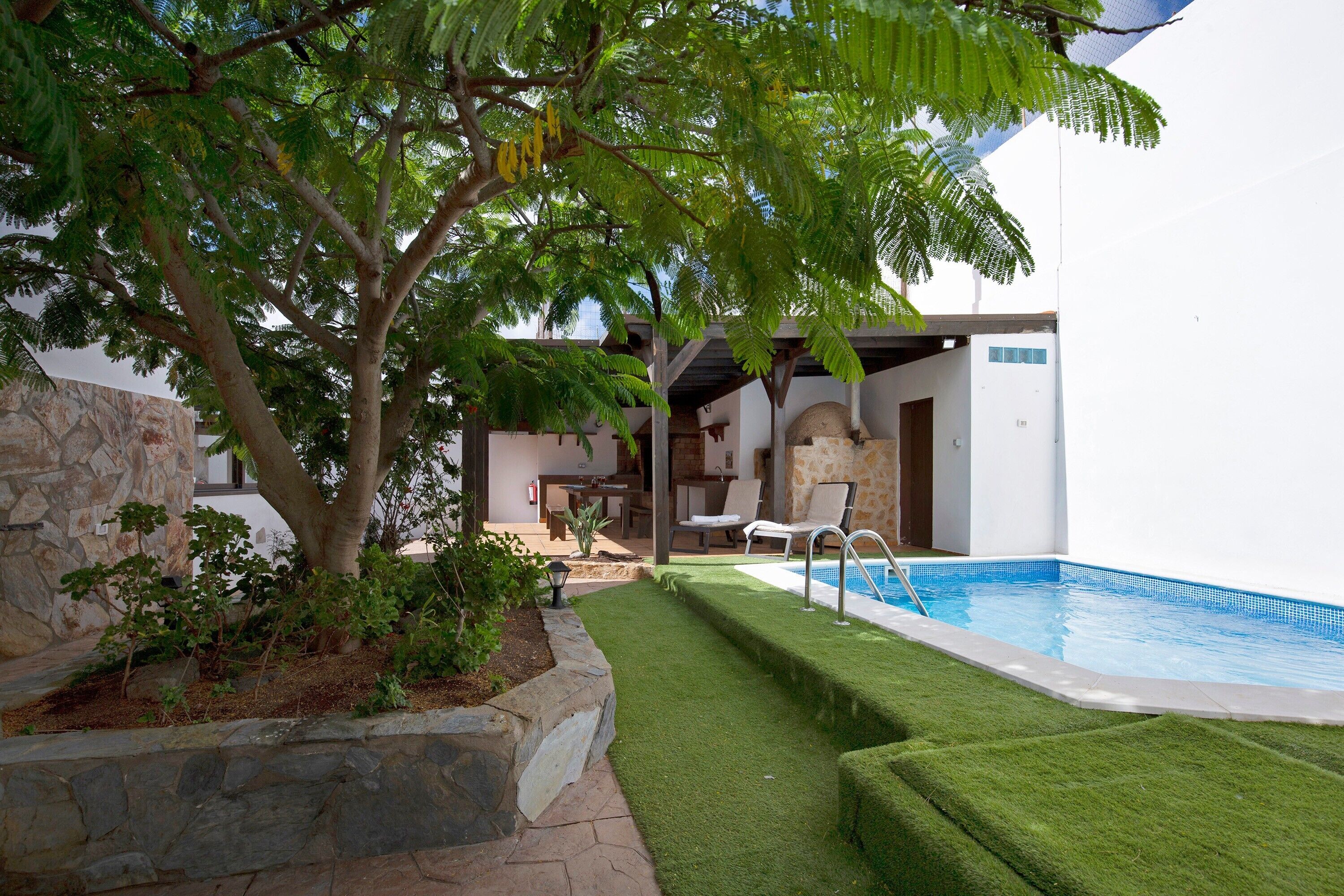 A pool area with artificial grass, a stone wall, and a tree.