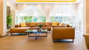 A modern living room with a brown leather sofa, a glass coffee table, and large windows with a view of greenery. - Villa 'El Coto' close to Fuengirola  (Mijas Costa)