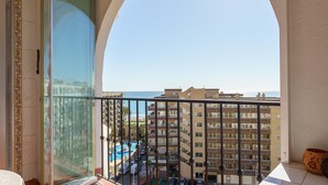 Un balcón con vista a una piscina y edificios, una puerta de cristal con un marco decorativo y una planta en maceta.