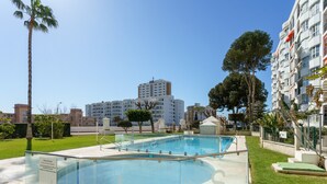 Una piscina con barrera de vidrio, rodeada de césped cuidado y árboles.