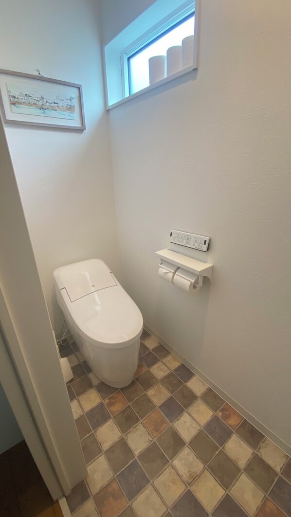 Ein kleines Badezimmer mit Toilette, einem Toilettenpapierhalter an der Wand und einem Fenster mit Blick zum Himmel.