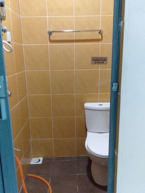 Une petite salle de bain fermée, équipée de toilettes, d’un sèche-mains et d’une pancarte indiquant qu’il faut tirer la chasse d’eau après utilisation.