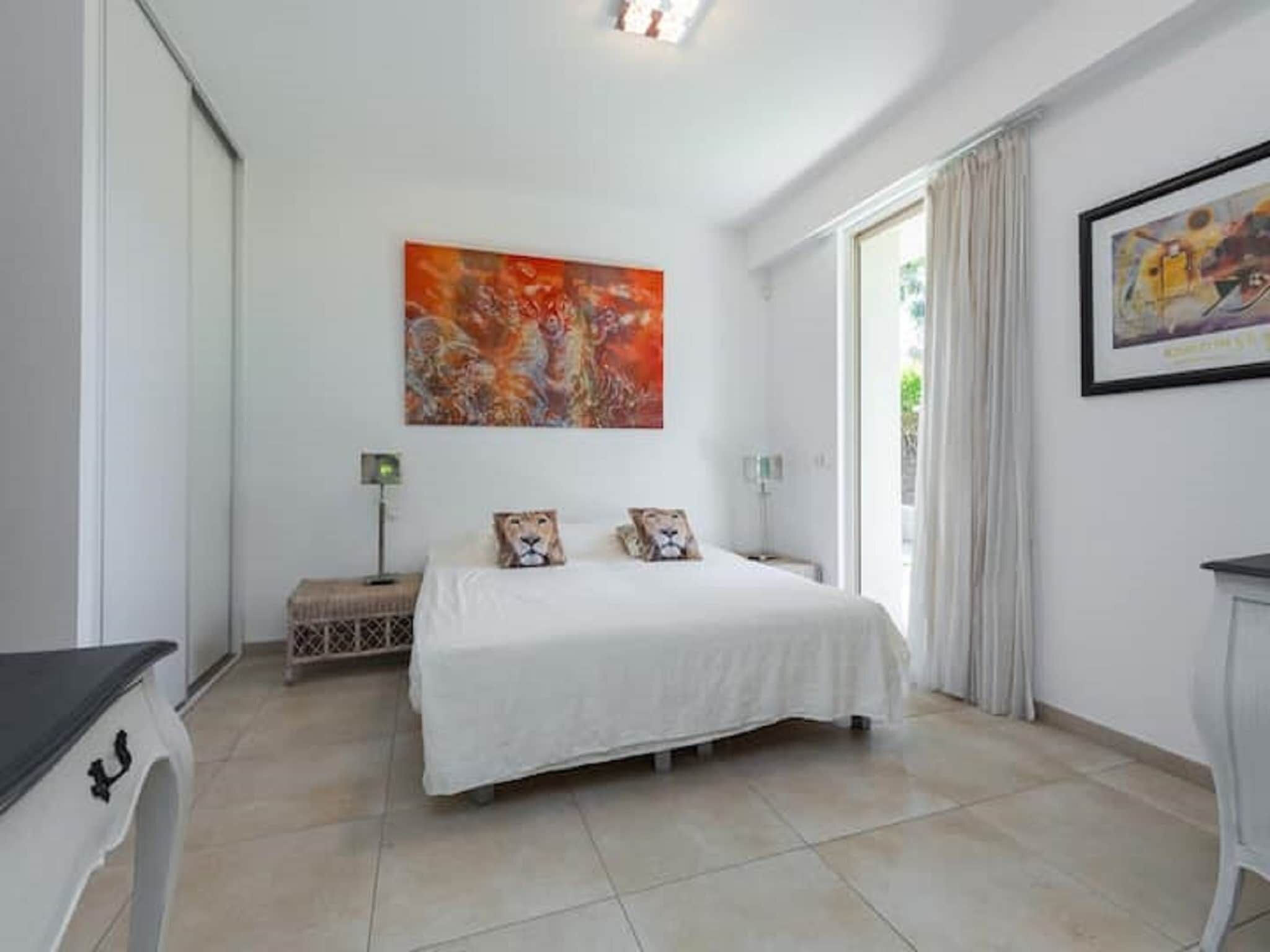 A bedroom with a bed, two pillows, a nightstand, a lamp, and a painting on the wall.