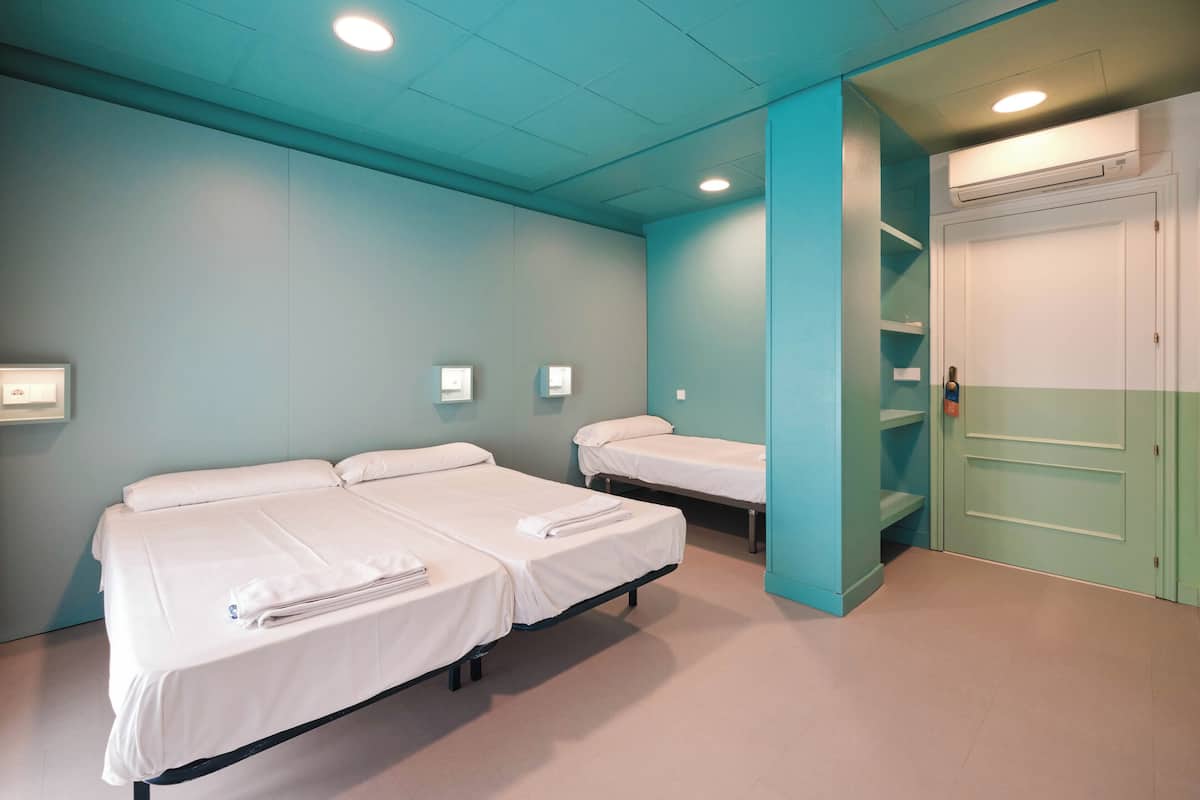 A room with two single beds, a white air conditioning unit, and a teal-colored door.