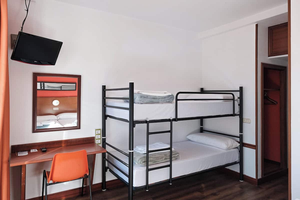 A bunk bed room with a desk and chair, a television mounted on the wall, and a wooden floor.