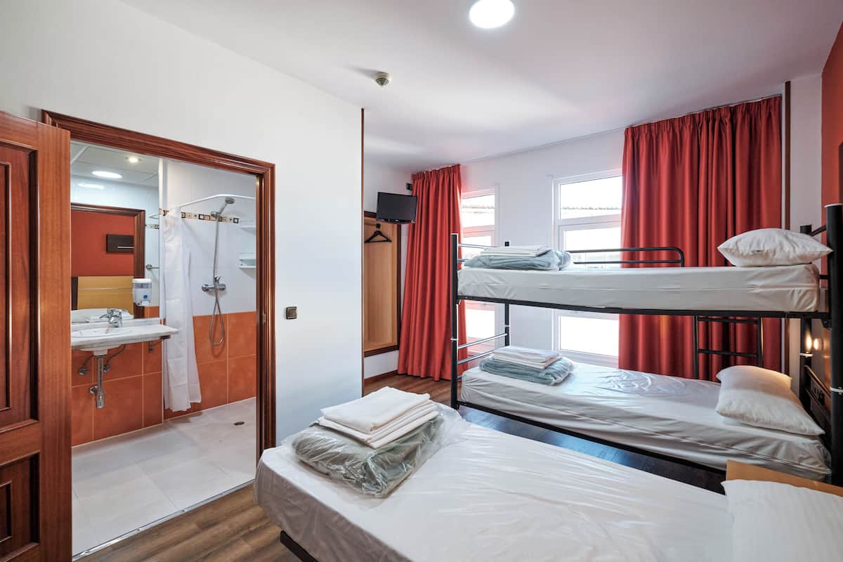 A room with a bunk bed, a shower area, a sink, and a TV.