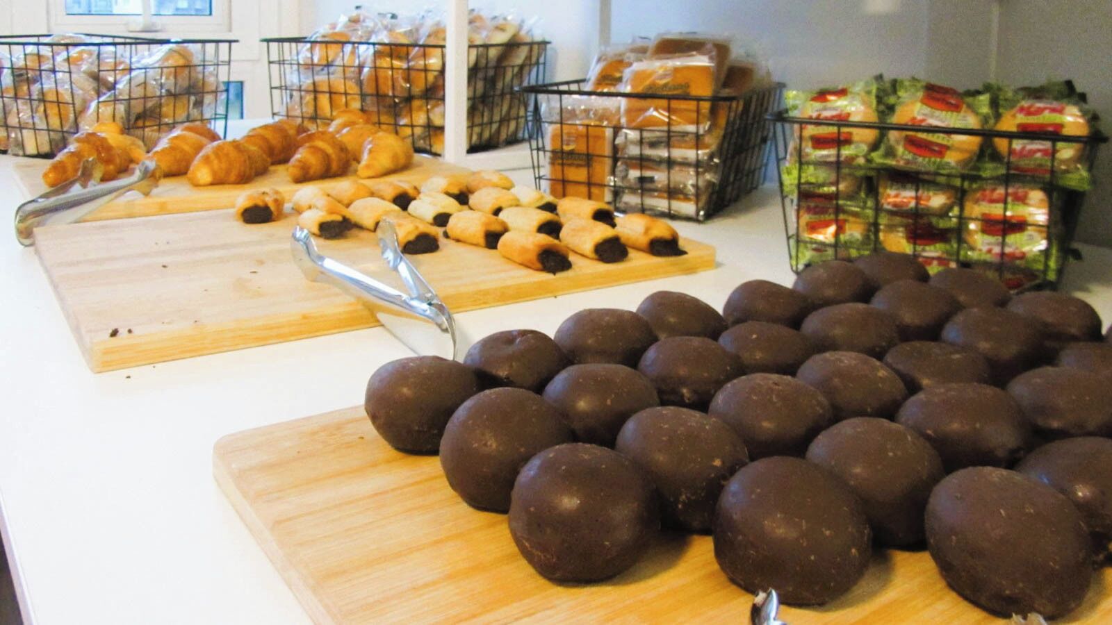 Mostrador de una panadería con una variedad de productos horneados, incluyendo croissants, dulces cubiertos de chocolate y pan empaquetado.