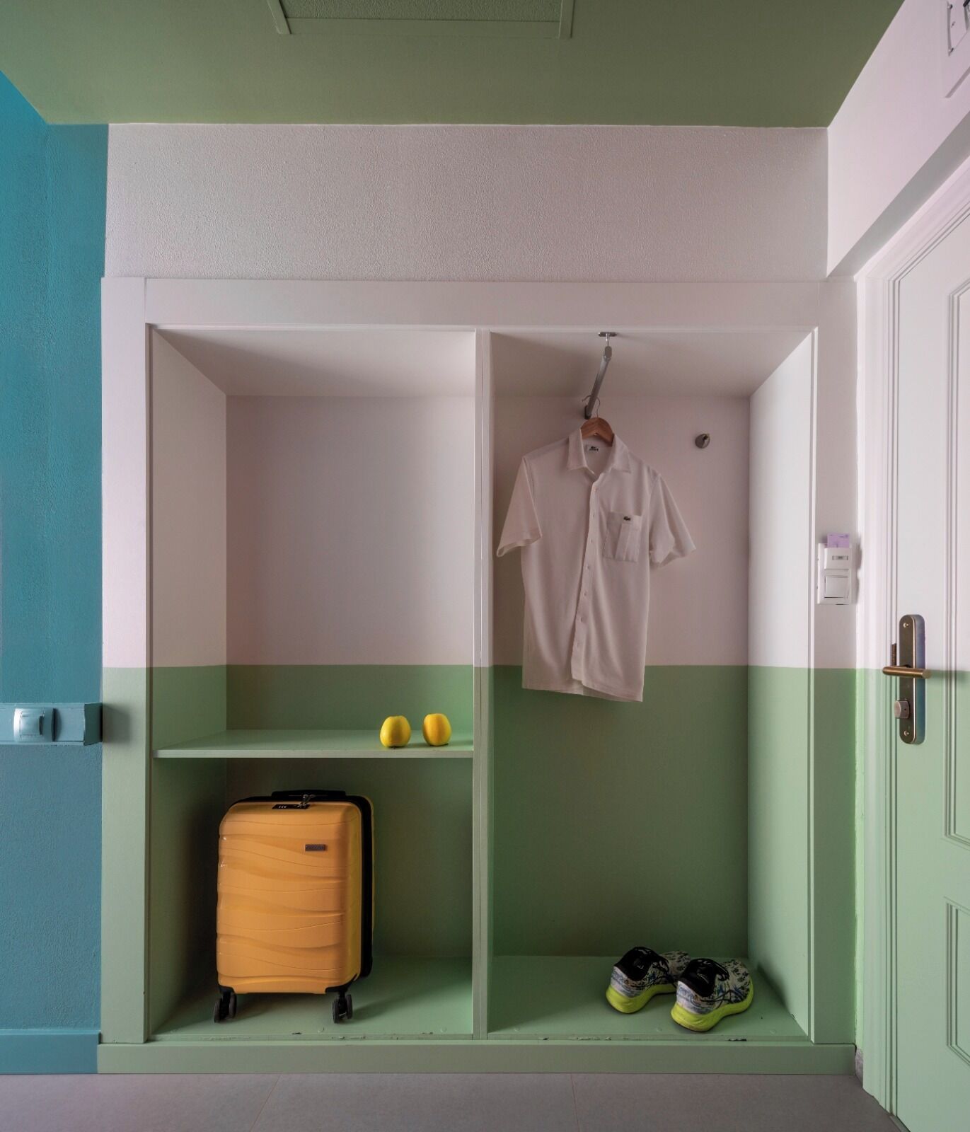 Une pièce aux couleurs vert et blanc, une valise, une paire de chaussures et un vêtement suspendu.