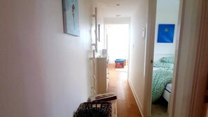Un pasillo estrecho con una mesa de madera y una cesta, que conduce a una habitación con una cama y un adorno azul en la pared.