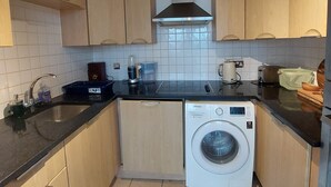 Cocina compacta con armarios de madera, lavadora integrada y cafetera.