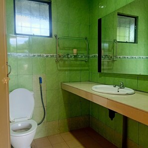 A bathroom with green tiles, a white toilet, a sink with a mirror, and a shower area. - OYO Home 90352 Muan's Homestay (Kota Belud)