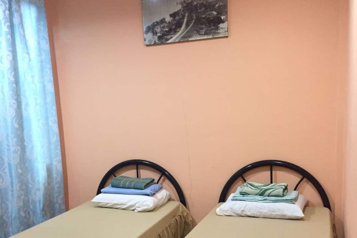 A room with two single beds, each with a beige bedspread and a matching skirt. There is a framed picture on the wall above the beds.