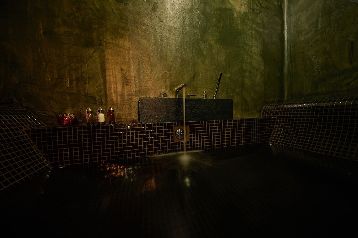 Une salle de bain faiblement éclairée, avec un sol carrelé, un lavabo avec un miroir et un porte-serviettes.