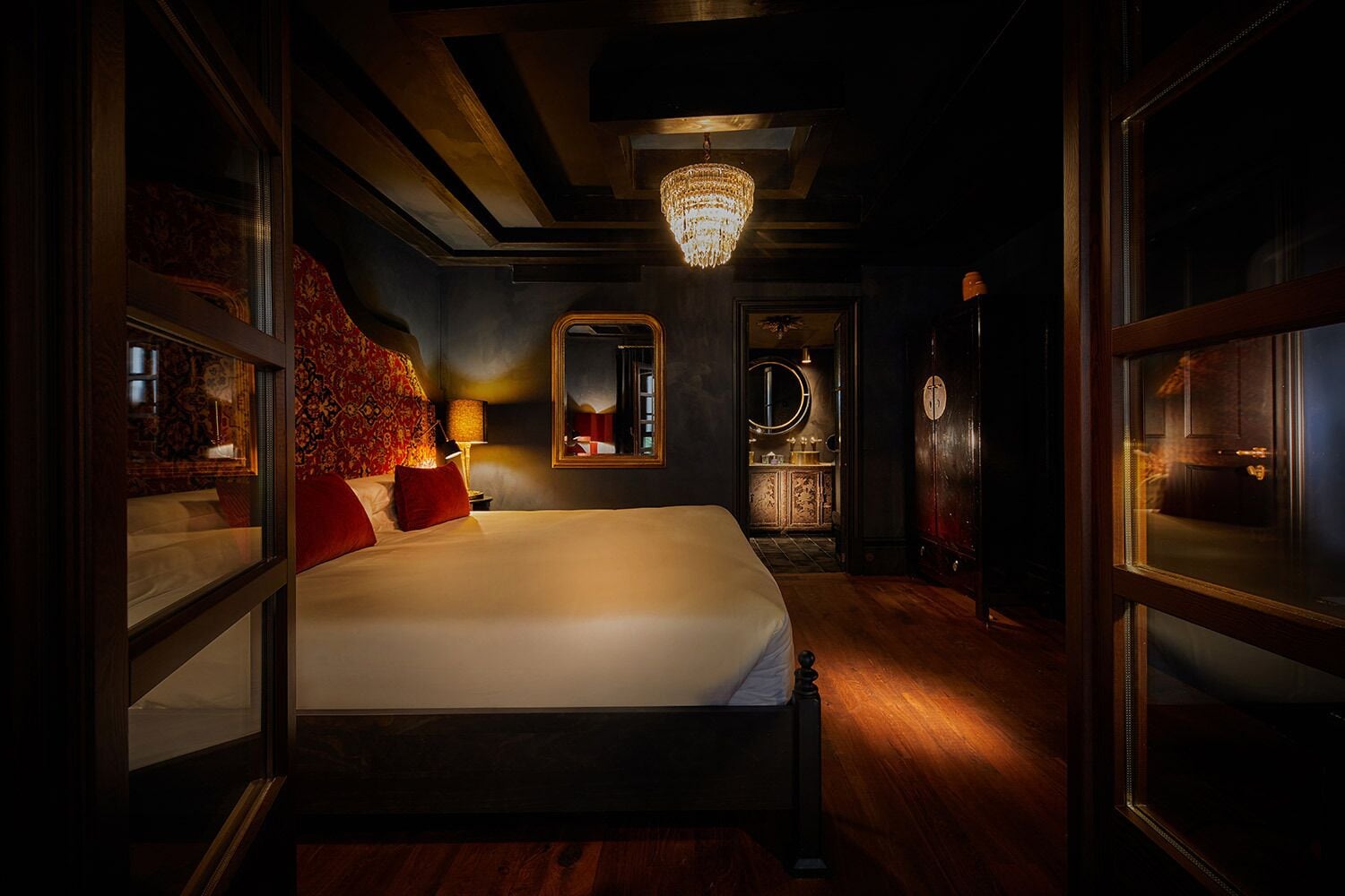 A dimly lit room with a large bed, a chandelier, and a mirror on the wall.