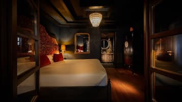 A dimly lit room with a large bed, a chandelier, and a mirror on the wall.