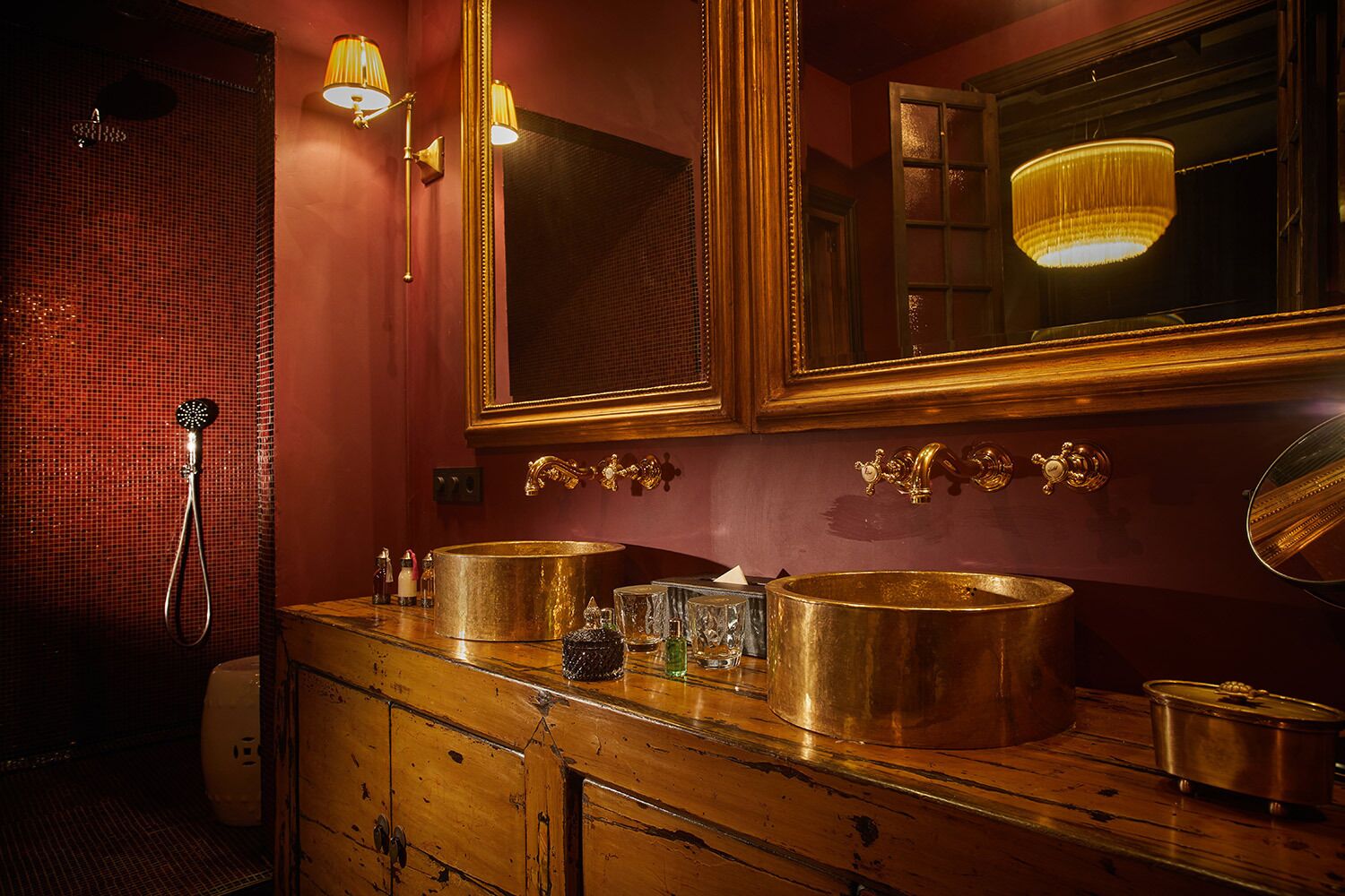 Un baño con tocador de madera, dos lavamanos dorados, un espejo grande y una ducha con cabezal dorado.
