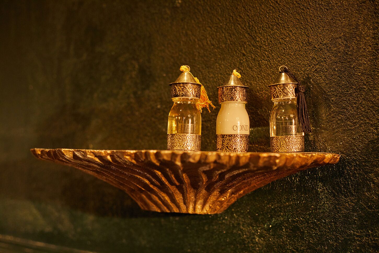 Three ornate bottles on a decorative tray against a textured wall.