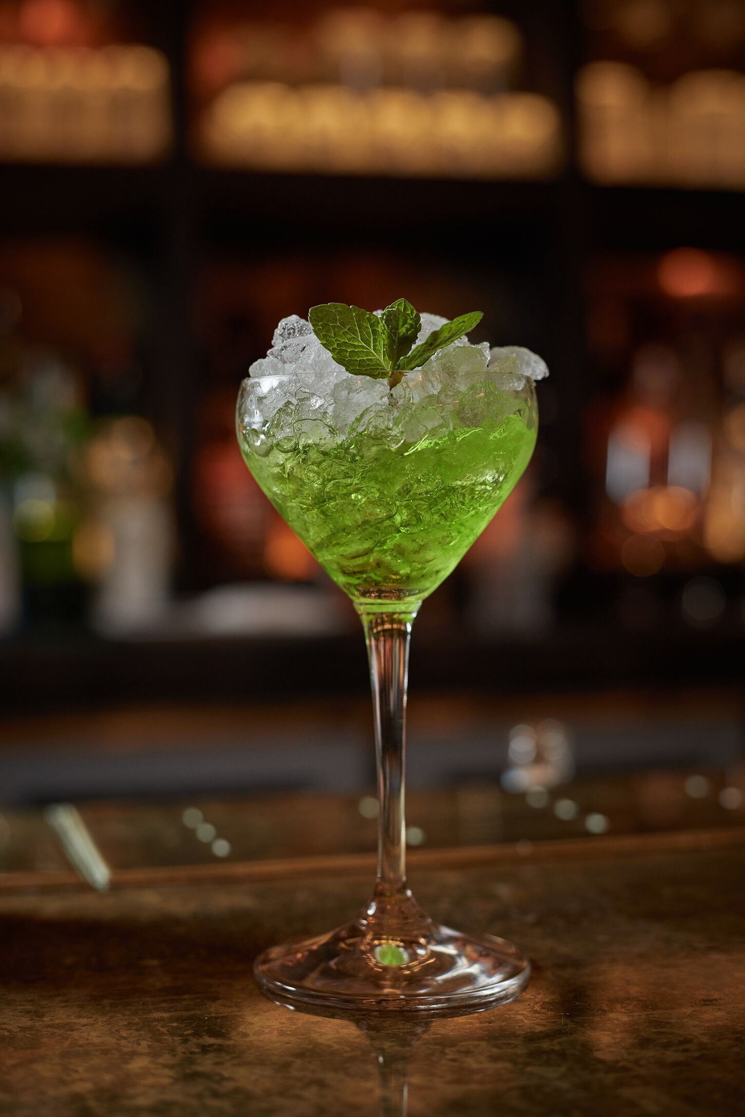 A cocktail glass with ice cubes and a mint leaf on a bar counter.