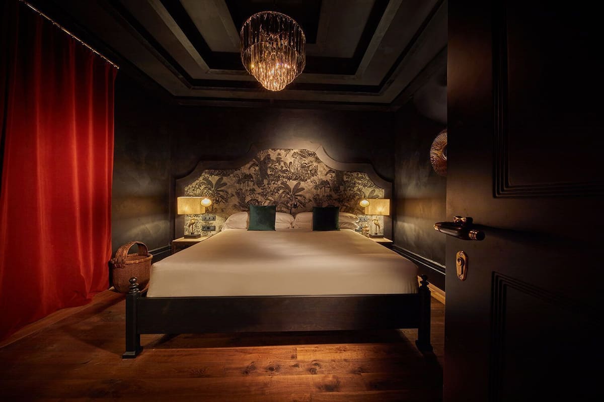 Une chambre à coucher avec un grand lit, deux tables de chevet avec des lampes, un lustre et un rideau rouge.