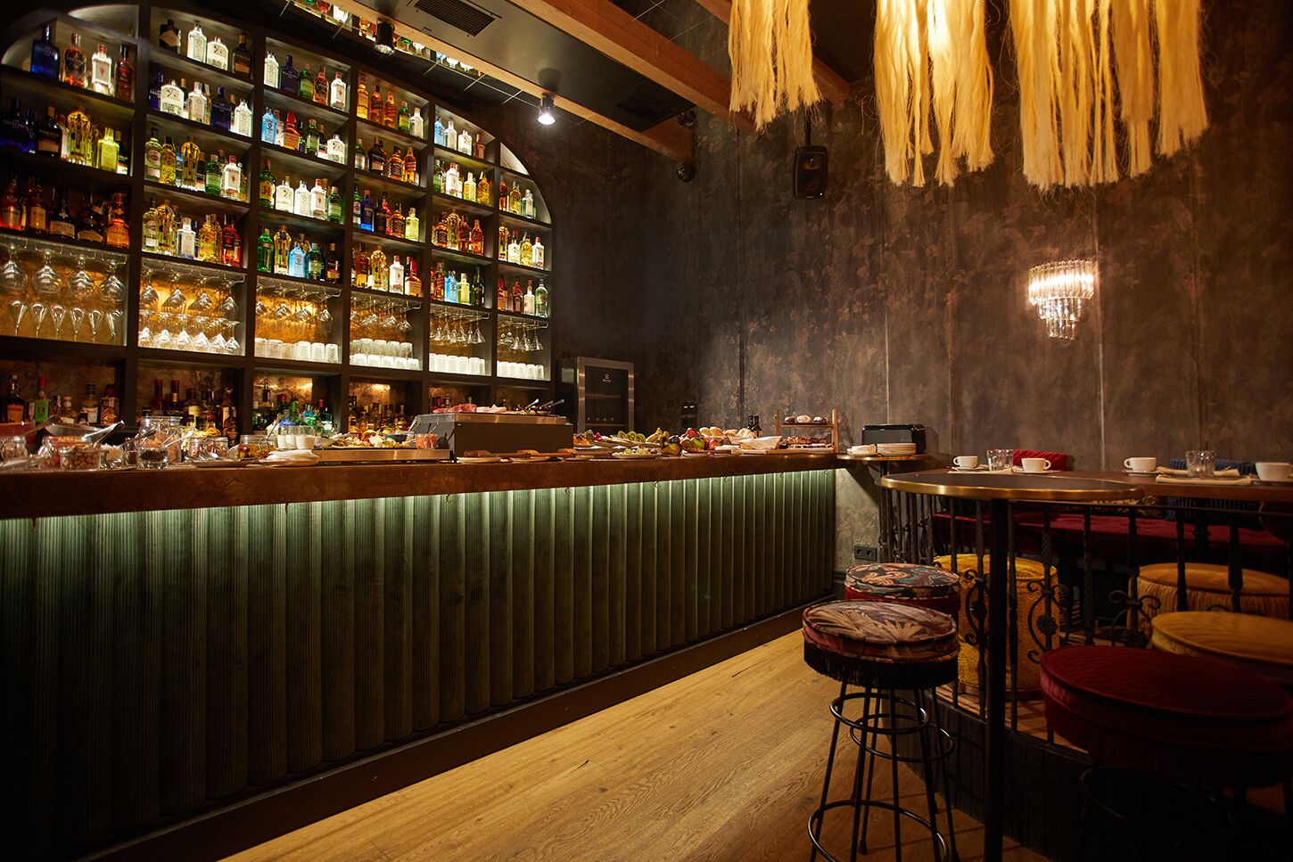 Zona de bar con mostrador de madera, estantes con botellas de licor y taburetes.