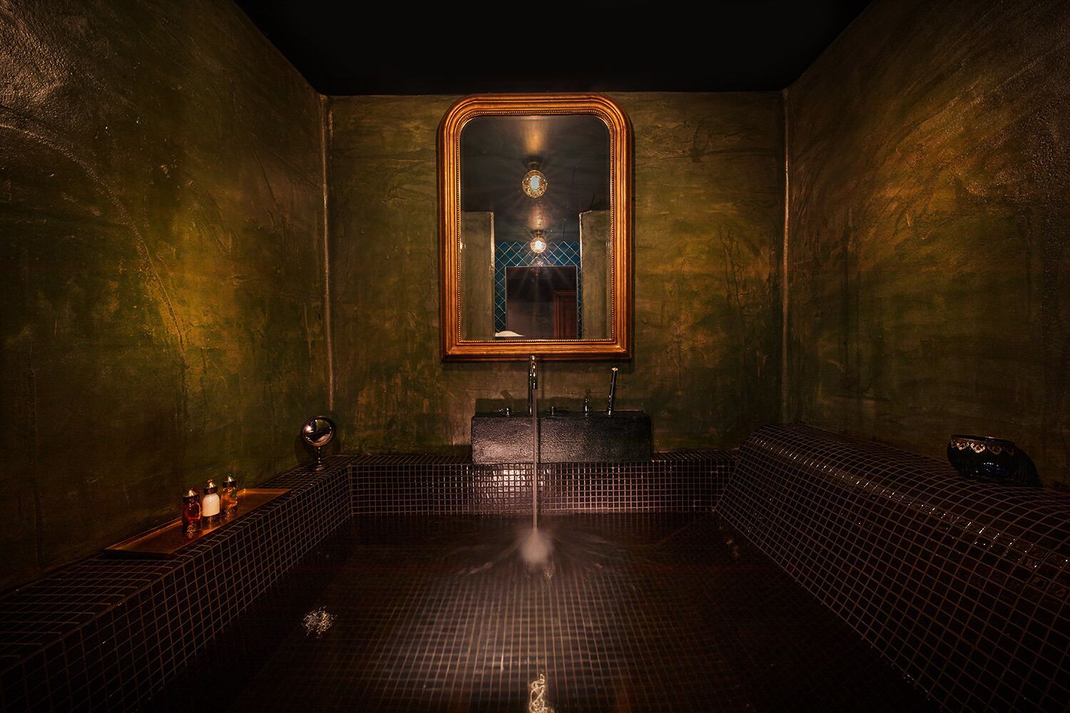 A spa room with a large mirror, a sink, and two seating areas.