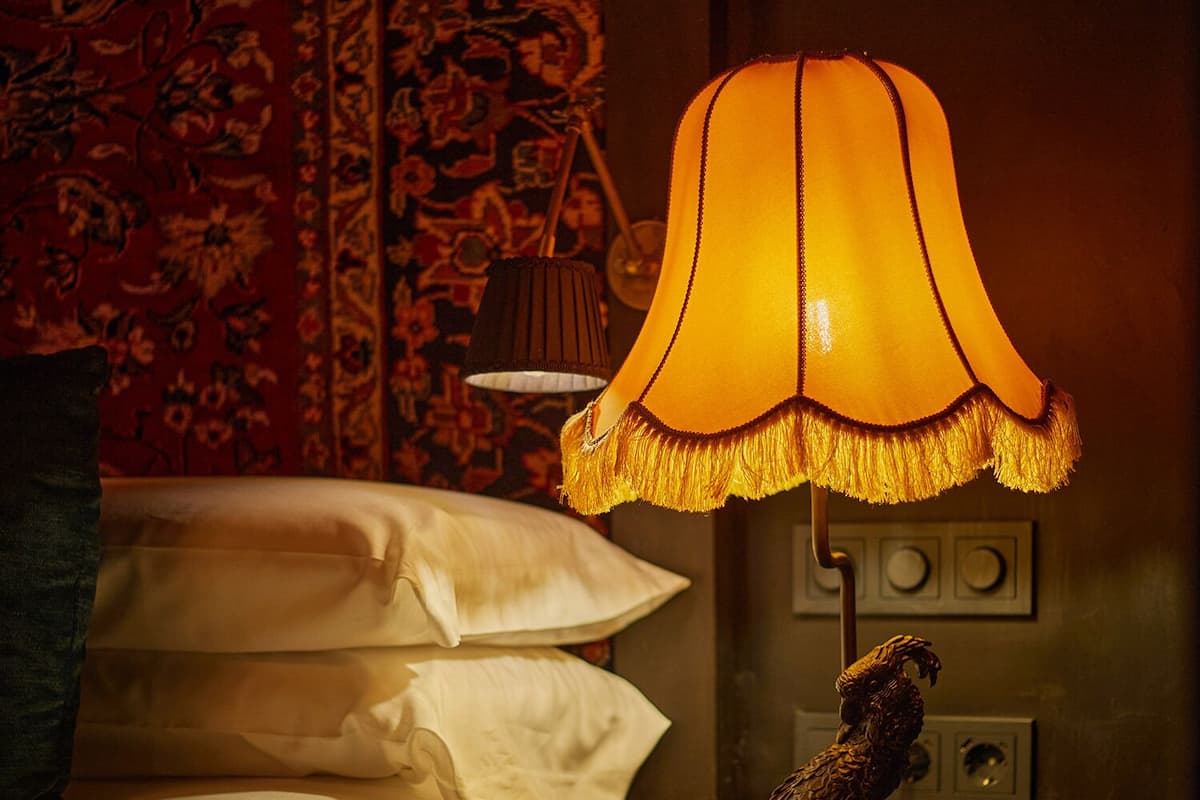 Un lit avec du linge de lit blanc, une lampe avec un abat-jour jaune et une petite table sur laquelle se trouve une statue.