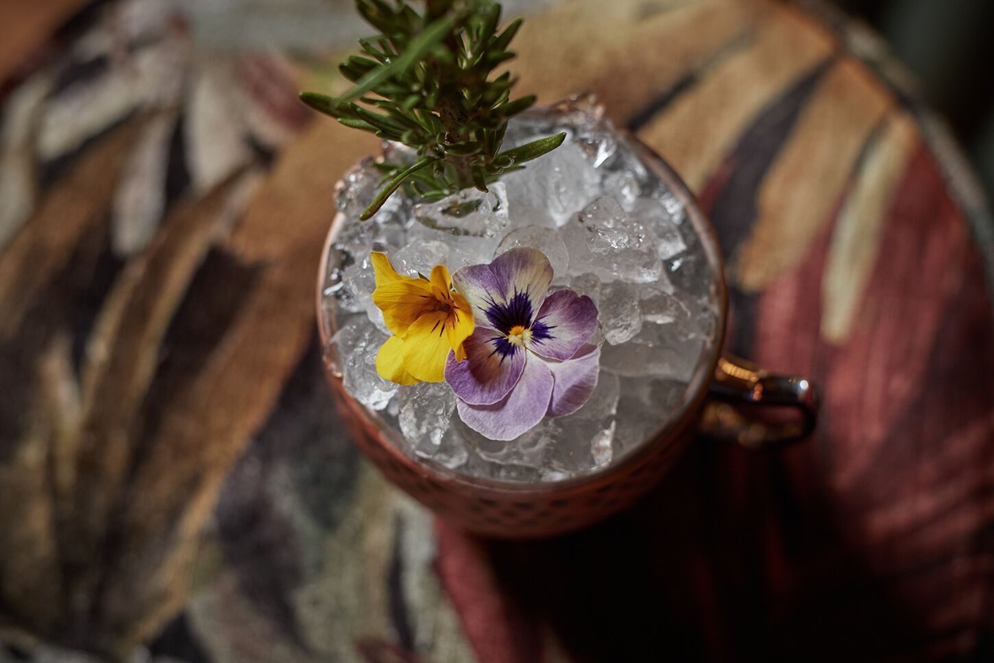 Ein Cocktail mit Eiswürfeln und Blüten auf einer Unterlage.