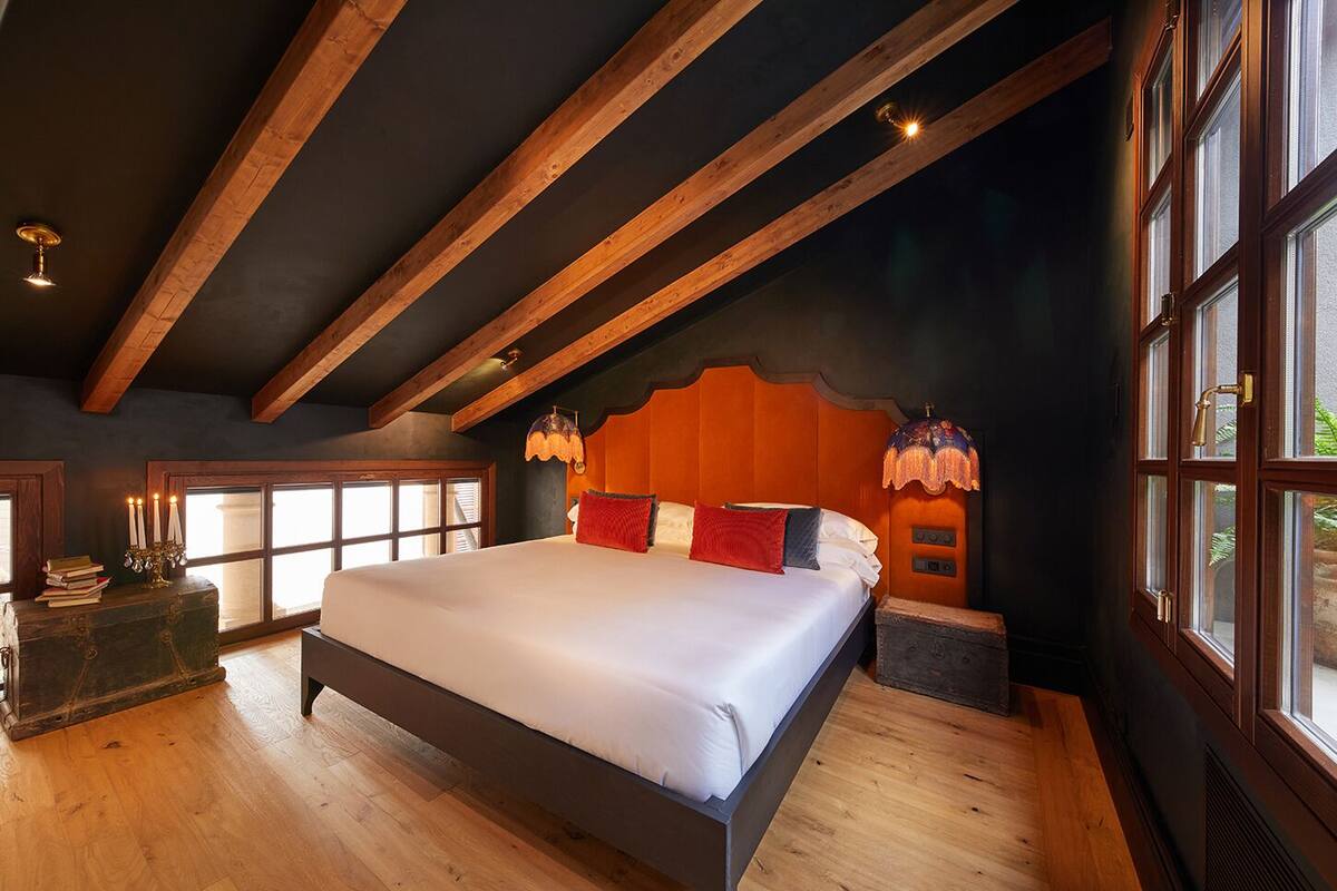 Une chambre spacieuse avec un grand lit, des poutres apparentes, une fenêtre offrant une belle vue et une table de chevet avec une lampe.